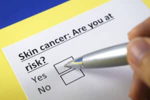 A close-up shot of a person checking a box on a form that says “Skin Cancer: Are You At Risk?